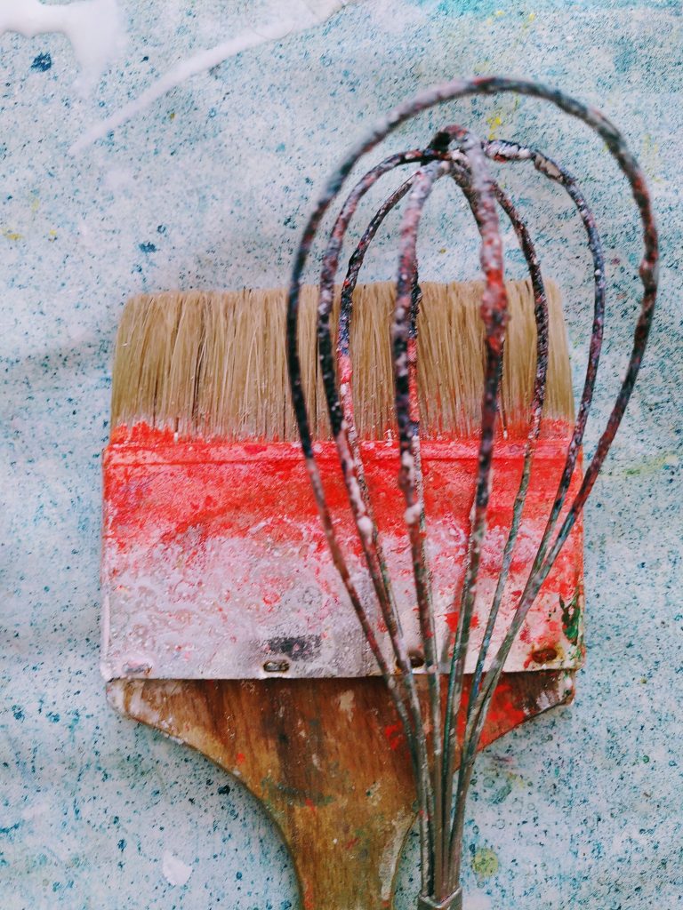 A brush and a whisk, both with paint on them