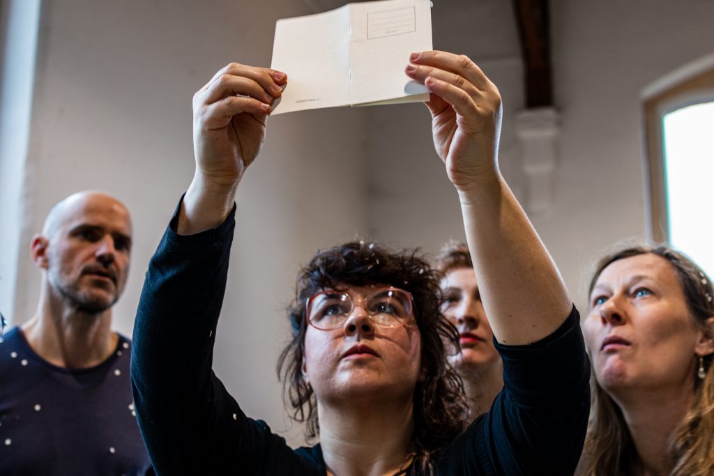 Performance Situation: Vier Menschen schauen auf zu einem papiernen Notizbuch, das eine der Personen hochhält