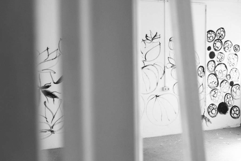der Blick durch eine Tür hindurch zeigt einen weißen Raum, dessen Wände mit schwarzen floralen Formen bemalt sind | the view through a door shows a white room with walls painted with black floral shapes