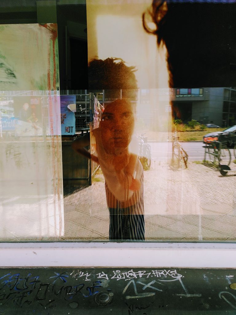 Ein Selfie, dass mit der Installation gemacht wurde. In der Schaufensterscheibe spiegelt sich schemenhaft eine Person. | A selfie that was taken with the installation. A person is reflected in the window pane.