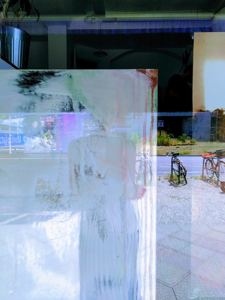 Ein Selfie, dass mit der Installation gemacht wurde. In der Schaufensterscheibe spiegelt sich schemenhaft eine Person. | A selfie that was taken with the installation. A person is reflected in the window pane.