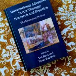 The book "International advances in art therapy research and practice" lying on a brown and white patterned blanket